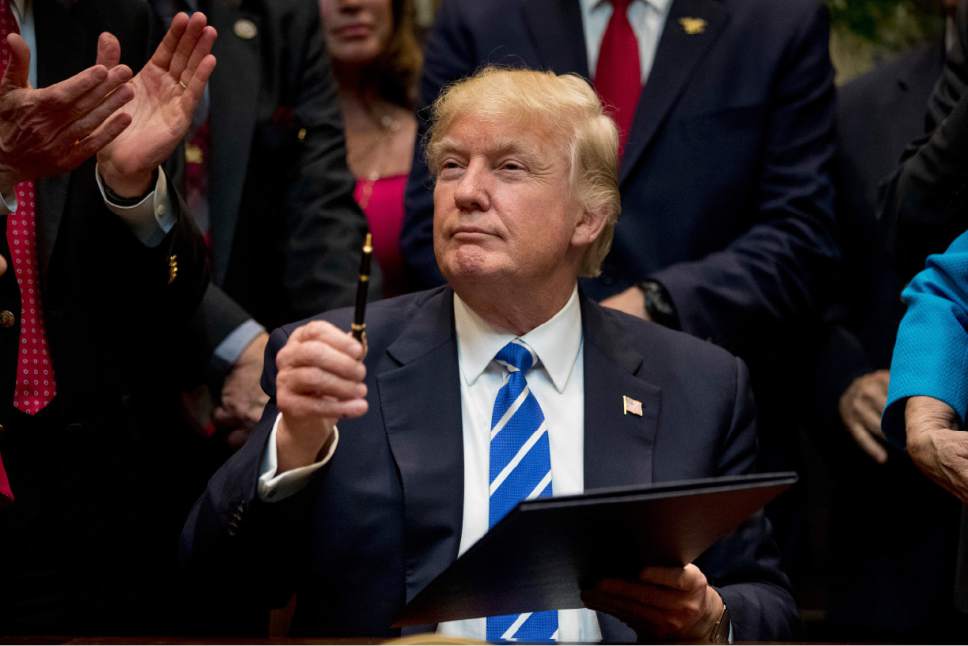 President Donald Trump holds up a pen he used to sign one of various bills in the Roosevelt Room of the White House, Monday, March 27, 2017, in Washington. (AP Photo/Andrew Harnik)
