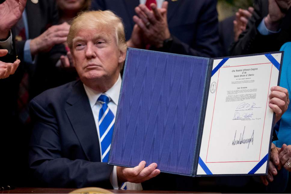 President Donald Trump holds up one of four bills during a signing ceremony in the Roosevelt Room of the White House in Washington, Monday, March 27, 2017. (AP Photo/Andrew Harnik)