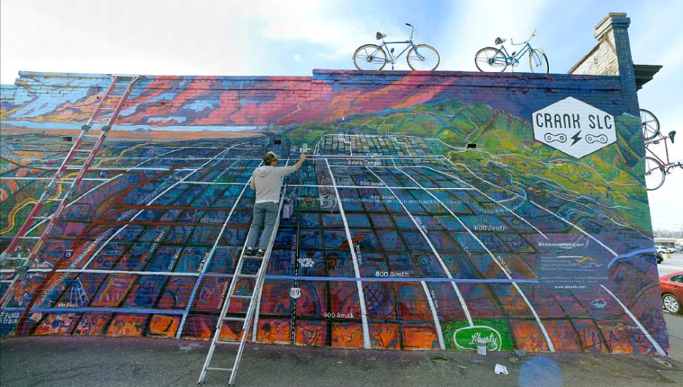 Al Hartmann  |  The Salt Lake Tribune
Artist Chris Peterson puts on finishing details of a vibrant new 54 x 20 foot mural showcasing Salt Lake Cityís bikeways at 750 South State Street Thursday April 6. 
The mural is a perspectival map of Salt Lake Cityís bikeways, featuring prominent city landmarks, the downtown and Wasatch skylines and the 9-Line Trail, Jordan River Parkway Trail and Bonneville Shoreline Trail. He started the mural last fall, was  halted by winter, and should be done in the next few days. 
 ìThe mural is meant to provide a bicycle-oriented perspective on the Salt Lake City landscape.  Downtown bike lanes connect to trails along the river and in the foothills," explains Peterson. ìThis artwork is about our cityís amazing landscape the growing bike infrastructure that spans it.î 
The SLC Bikeways Mural Project was made possible through support and collaboration with Crank SLC owners Christian Clemens and Juliet Lalouel, Bike Utah, and multimedia artist Patrick Clifford. The project also received support from the Utah Division of Arts and Museumsí ìRandom Acts of Artî grant program.