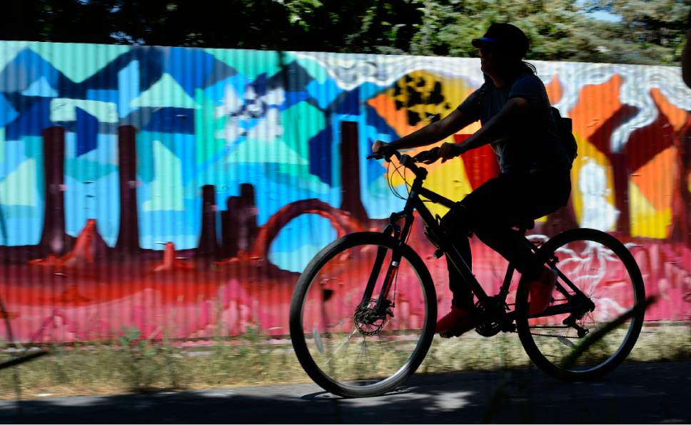 Scott Sommerdorf | The Salt Lake Tribune
A bicyclist passes by the panel that contains art that local artists with Justified Ink and Glendale Middle School students installed on a length of fence next to the Jordan Parkway Trail, Friday, June 2, 2017.