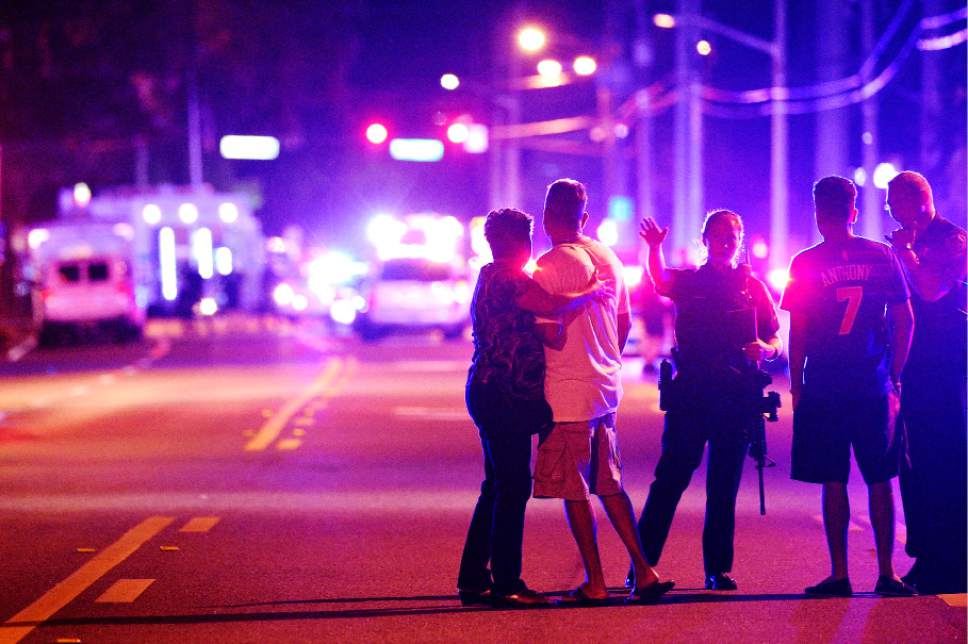 FILE - In this June 12, 2016, file photo an Orlando Police officers direct family members away from a fatal shooting at Pulse nightclub in Orlando, Fla. Church bells will toll throughout the Orlando area as residents reflect on the 49 patrons killed during a massacre at the gay nightclub Pulse in the worst mass shooting in recent U.S. history. Starting in the wee hours Monday, June 12, 2017, and continuing almost 24 hours later, survivors, victims' families, city officials and central Florida residents will remember the victims with multiple services. (AP Photo/Phelan M. Ebenhack, File)