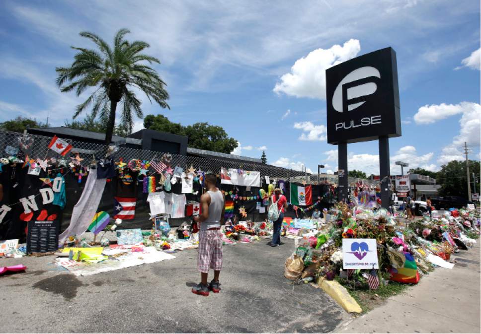 FILE - This July 11, 2016, file photo, visitors gather at a makeshift memorial outside the Pulse nightclub in Orlando, Fla. Church bells will toll throughout the Orlando area as residents reflect on the 49 patrons killed during a massacre at the gay nightclub Pulse in the worst mass shooting in recent U.S. history. Starting in the wee hours Monday, June 12, 2017, and continuing almost 24 hours later, survivors, victims' families, city officials and central Florida residents will remember the victims with multiple services. (AP Photo/John Raoux, File)