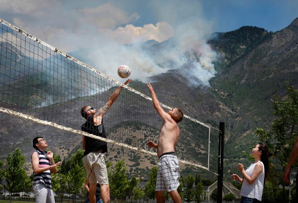 Scott Sommerdorf   |  The Salt Lake Tribune  
The Victor family plays volleyball as aerial crews fight the fires being driven uphill as seen from Creekside Park in Alpine, Sunday, July 16, 2017.